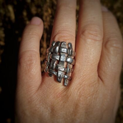 Close-up van de zilveren ring Textum, met de hand geweven met een uniek, complex vlechtwerkpatroon, gedragen op een vinger.