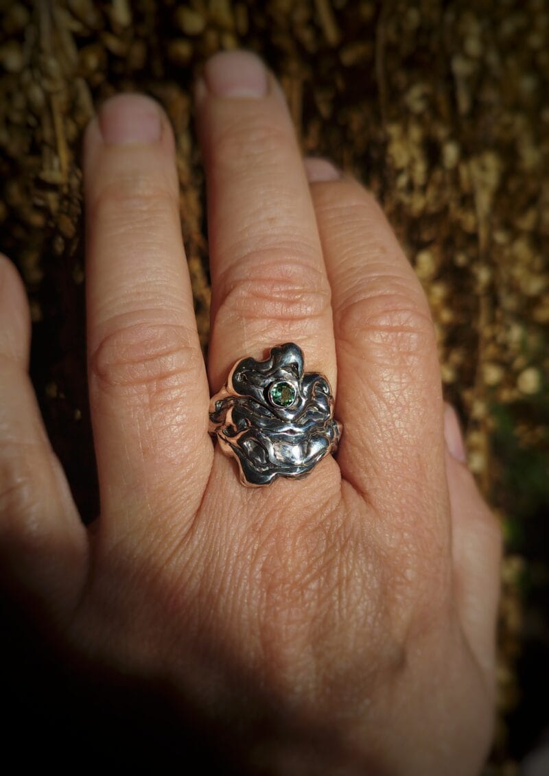 Een handgemaakte zilveren ring met een organisch, golvend design waarin een kleine, ronde, gefacetteerde chrysopraas is gezet.