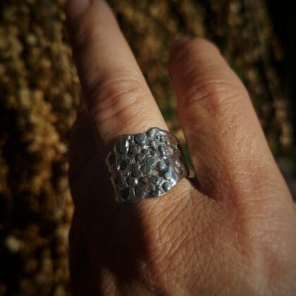Een brede, handgemaakte zilveren ring met een abstract, bubbel-achtig patroon van zowel dichte als opengewerkte vormen.