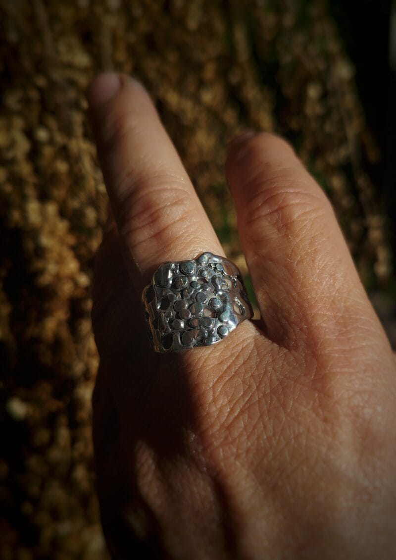 Een brede, handgemaakte zilveren ring met een abstract, bubbel-achtig patroon van zowel dichte als opengewerkte vormen.
