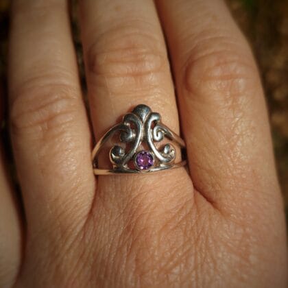 Zilveren ring met een tiara-vormig, opengewerkt design, waarin een kleine ronde, gefacetteerde amethist is gezet.