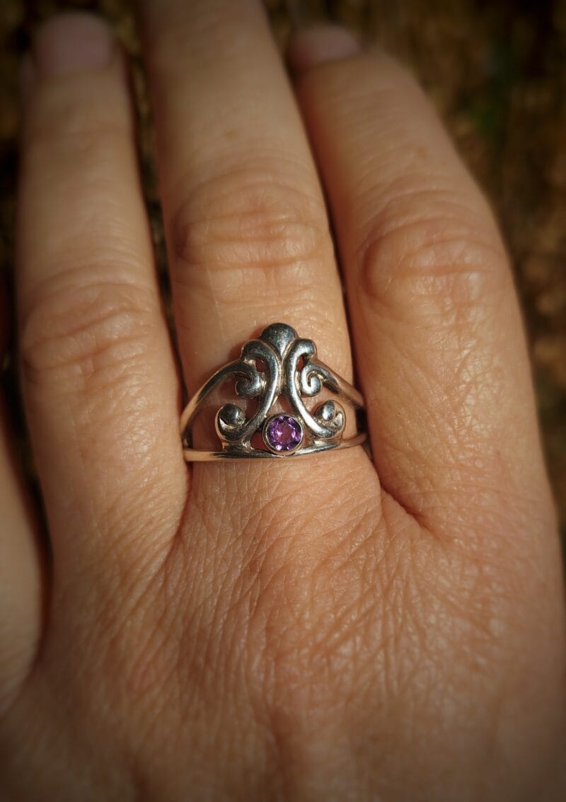 Zilveren ring met een tiara-vormig, opengewerkt design, waarin een kleine ronde, gefacetteerde amethist is gezet.