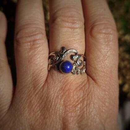 Zilveren ring met een diepblauwe, ronde lapis lazuli cabochon, gezet in een organisch, abstract zilveren bandje met krullende patronen.