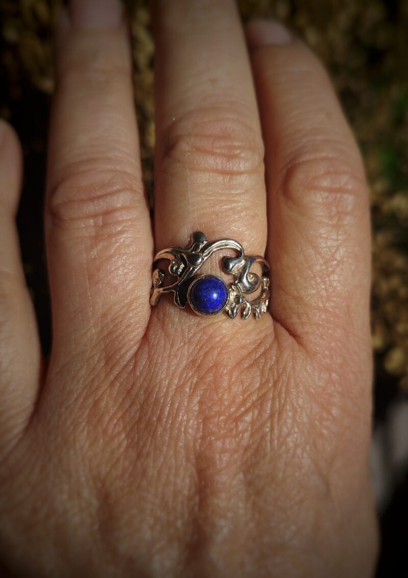 Zilveren ring met een diepblauwe, ronde lapis lazuli cabochon, gezet in een organisch, abstract zilveren bandje met krullende patronen.