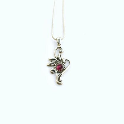 Een handgemaakte zilveren ketting met een bloem-achtig hangertje en een roos geslepen, ronde rode granaat in het midden.