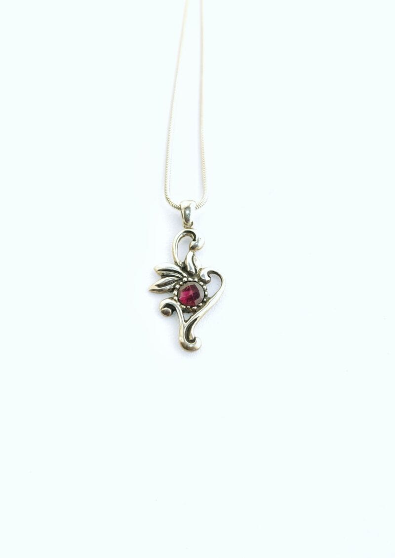 Een handgemaakte zilveren ketting met een bloem-achtig hangertje en een roos geslepen, ronde rode granaat in het midden.